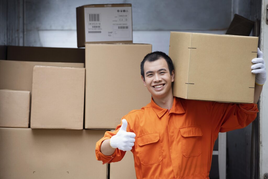 This image shows a warehouse worker carrying a package with confidence and giving a thumbs-up—symbolizing efficiency, accuracy, and satisfaction.
