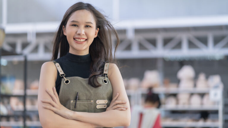 Asia female ceramist with apron hand confident chest in her workshop clay sculpture studio with positive smiling warm welcome ready to start new factory ceramic workshop with new collection of work