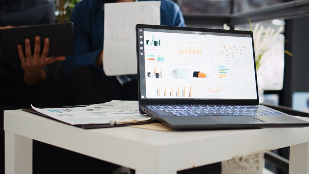 Two coworkers planning new strategy and analyzing online company information in startup office. Business partners collaborating on analytics presentation, using laptop and papers.