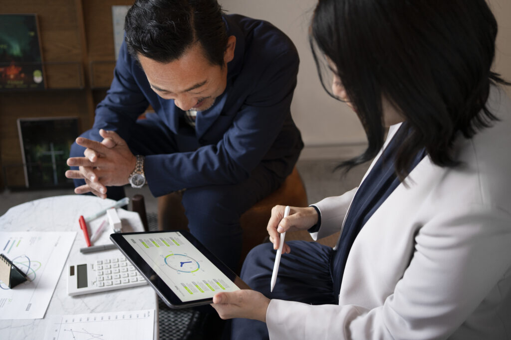 Two business professionals reviewing financial data on a tablet, discussing analytics and performance metrics in a meeting setting.