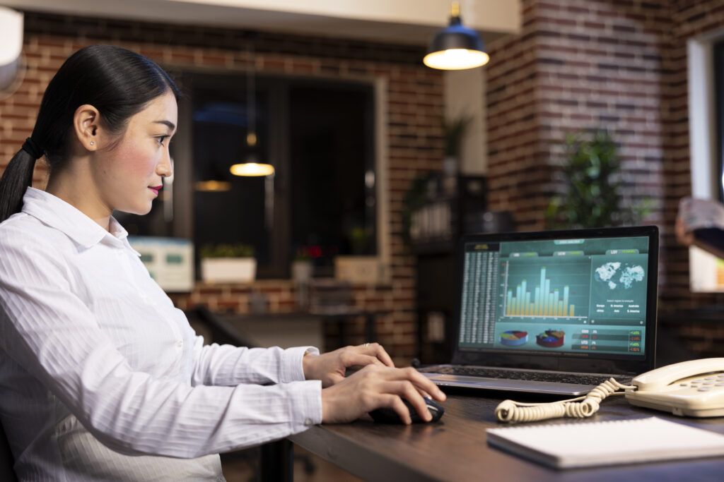 Businesswoman analyzing company performance data on a laptop with charts and graphs in a modern office environment.